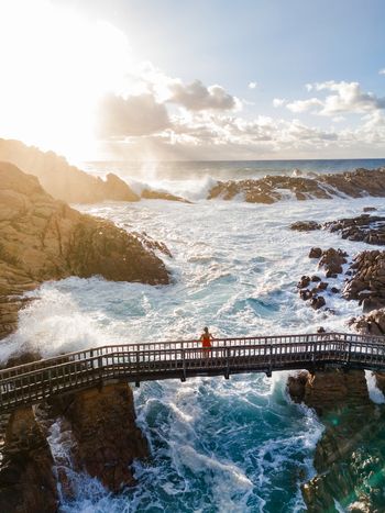Aerial view of Canal Rocks Bridge with a person standing on the wooden walkway above crashing waves and rocky coastline in Yallingup Western Australia Australia. Aerial view of Canal Rocks Bridge with a person standing on the wooden walkway above crashing waves and rocky coastline in Yallingup Western Australia Australia.