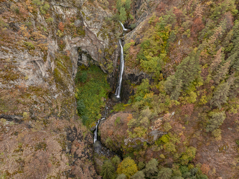 Aerial view of Ovcharenski Waterfall Goritsa cascading down a rocky cliff surrounded by autumn foliage and dense forest in Ovchartsi Kyustendil Province Bulgaria. Aerial view of Ovcharenski Waterfall Goritsa cascading down a rocky cliff surrounded by autumn foliage and dense forest in Ovchartsi Kyustendil Province Bulgaria.