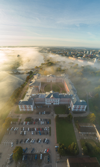 Aerial view of Jelgava Palace surrounded by morning mist lush trees and a parking lot in Jelgava Latvia. Aerial view of Jelgava Palace surrounded by morning mist lush trees and a parking lot in Jelgava Latvia.