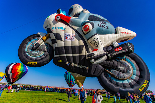 Albuquerque United States 09 October 2017 View of a motorcycle shaped hot air balloon soaring high above the vibrant green field a spectacle of color against the clear blue sky.