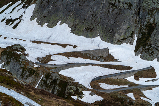 View of the winding Tremola road at Sankt Gotthard Pass with patches of snow and steep rocky cliffs in Airolo Ticino Switzerland.