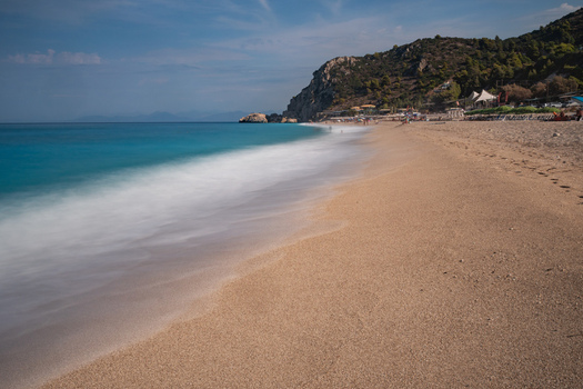 View of turquoise waters meet the golden sands under a vast sky where the beach stretches towards a distant verdant cliff Kathisma Lefkada Greece. View of turquoise waters meet the golden sands under a vast sky where the beach stretches towards a distant verdant cliff Kathisma Lefkada Greece.