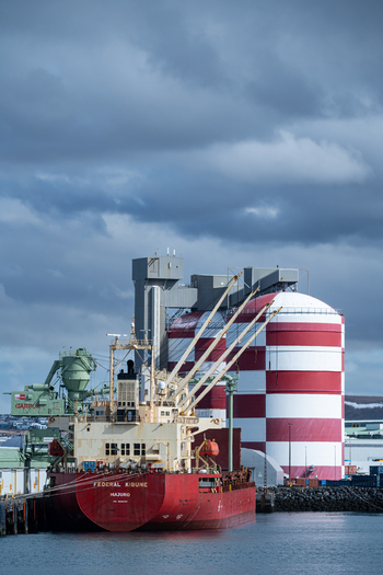 Hafnarfjordur Iceland 17 April 2026 View of the cargo ship Federal Kibune docked at the port next to a large red and white striped industrial silo under a cloudy sky.