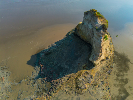 Aerial view of a unique coastal rock formation rising from the sandy beach with textured surfaces and shadows cast on the shore in Bali Indonesia. Aerial view of a unique coastal rock formation rising from the sandy beach with textured surfaces and shadows cast on the shore in Bali Indonesia.