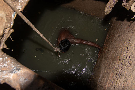 Dhaka Bangladesh 18 April 2018 View of a manual sewer cleaner working inside a dark narrow manhole filled with murky water and brick walls. Dhaka Bangladesh 18 April 2018 View of a manual sewer cleaner working inside a dark narrow manhole filled with murky water and brick walls.