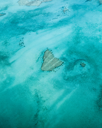Aerial view of the shallow turquoise waters surrounding a small heart shaped island creating a striking contrast between the light sand and deep blue hues Noumea South Province New Caledonia.