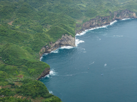 Aerial view of green cliffs meeting the deep blue ocean with white waves crashing below Gunungkidul Regency Special Region of Yogyakarta Indonesia. Aerial view of green cliffs meeting the deep blue ocean with white waves crashing below Gunungkidul Regency Special Region of Yogyakarta Indonesia.