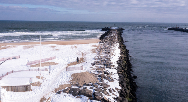 Aerial view of the snow covered beach and stone jetty at Manasquan Inlet with ocean waves and a couple walking along the shoreline in Manasquan New Jersey United States. Aerial view of the snow covered beach and stone jetty at Manasquan Inlet with ocean waves and a couple walking along the shoreline in Manasquan New Jersey United States.