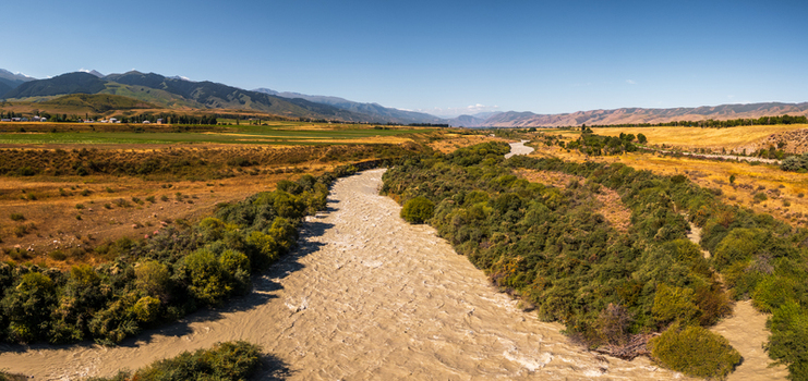 Aerial view of the Chon Kemin river flowing through a valley with lush green vegetation golden fields and distant mountains in Kemin Chuy Province Kyrgyzstan.