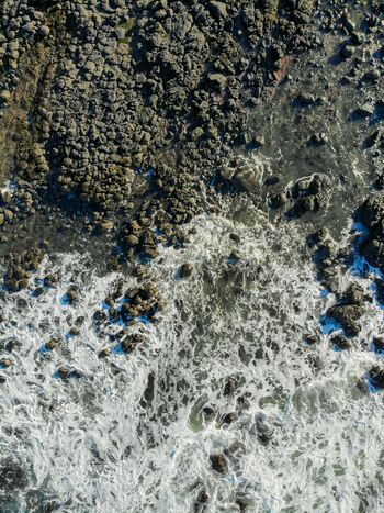 Aerial view of waves crashing against dark basalt rocks along the rugged coastline in Coleraine Northern Ireland United Kingdom. Aerial view of waves crashing against dark basalt rocks along the rugged coastline in Coleraine Northern Ireland United Kingdom.