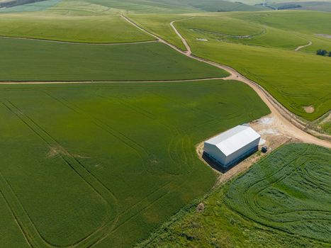 Aerial view of a white agricultural shed surrounded by vast green fields and winding dirt roads in Greyton Western Cape South Africa.