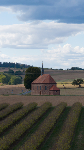 Aerial view of Wendelinuskapelle surrounded by agricultural fields and rows of crops under a cloudy sky in Dieburg Hessen Germany. Aerial view of Wendelinuskapelle surrounded by agricultural fields and rows of crops under a cloudy sky in Dieburg Hessen Germany.