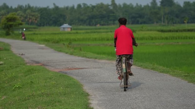 View of a man riding a bicycle on a rural road Bangladesh.