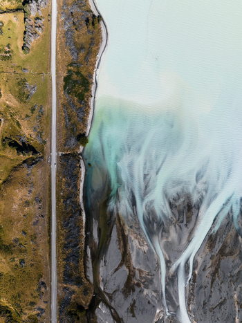 Aerial view of turquoise waters merging with sandy shores creating intricate patterns alongside a straight road Lake Tekapo Canterbury Region New Zealand. Aerial view of turquoise waters merging with sandy shores creating intricate patterns alongside a straight road Lake Tekapo Canterbury Region New Zealand.