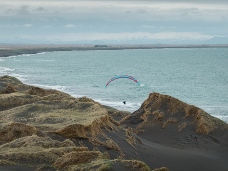 Aerial view of a paraglider soaring over the black sand dunes of Hafnarskeidh with the ocean and distant mountains in the background in Sveitarfelagid Olfus Iceland. Aerial view of a paraglider soaring over the black sand dunes of Hafnarskeidh with the ocean and distant mountains in the background in Sveitarfelagid Olfus Iceland.