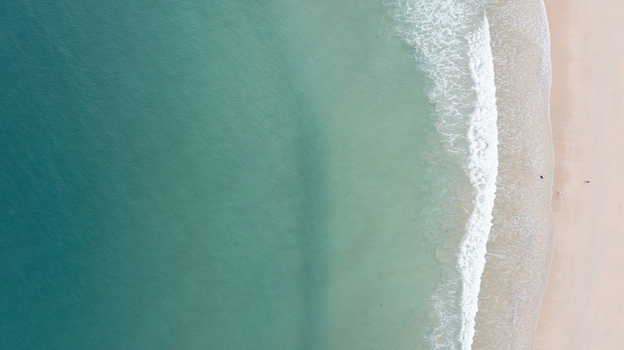 Aerial view of Harlyn Bay Beach featuring turquoise water and white waves crashing onto the sandy shore with tiny figures walking in Saint Merryn Cornwall United Kingdom.