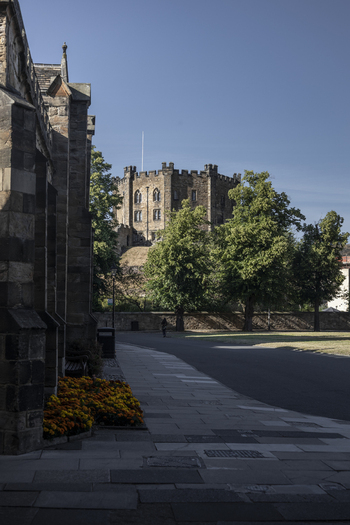 View of the historic Durham Castle rising above lush green trees and a paved path in Durham England United Kingdom. View of the historic Durham Castle rising above lush green trees and a paved path in Durham England United Kingdom.