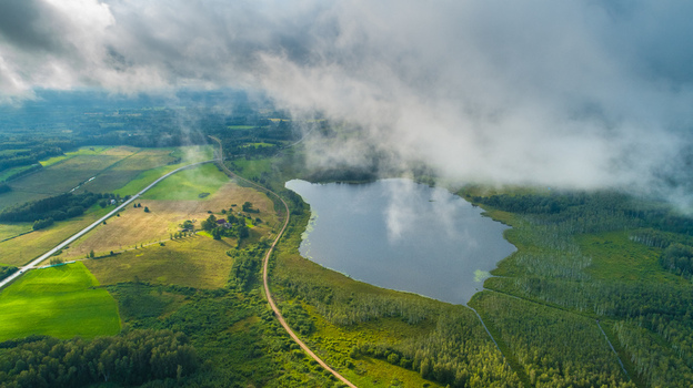 Aerial view of a serene lake surrounded by lush green forests agricultural fields and a winding road in Latvia. Aerial view of a serene lake surrounded by lush green forests agricultural fields and a winding road in Latvia.