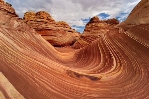 View of the swirling sandstone patterns and undulating rock formations of The Wave under a cloudy sky in Kanab Arizona United States. View of the swirling sandstone patterns and undulating rock formations of The Wave under a cloudy sky in Kanab Arizona United States.