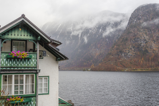 View of a traditional Alpine house with a green wooden balcony overlooking the calm lake and mist covered mountains in Hallstatt Upper Austria Austria. View of a traditional Alpine house with a green wooden balcony overlooking the calm lake and mist covered mountains in Hallstatt Upper Austria Austria.