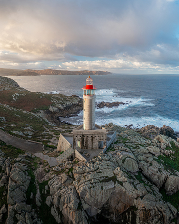 Aerial view of Faro de Punta Nariga lighthouse standing on rugged granite rocks with crashing waves and a cloudy sky in Malpica A Coruna Spain. Aerial view of Faro de Punta Nariga lighthouse standing on rugged granite rocks with crashing waves and a cloudy sky in Malpica A Coruna Spain.