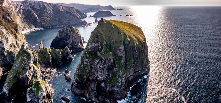 Aerial view of the dramatic cliffs and rock formations at Glenlough Bay with sunlight reflecting on the Atlantic Ocean in Ardara County Donegal Ireland.