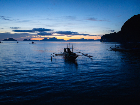 Aerial view of traditional outrigger boats anchored on calm water during twilight with silhouetted islands in the background El Nido Mimaropa Philippines.