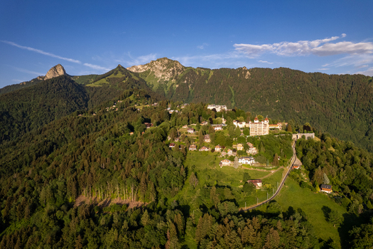 Aerial view of Glion village nestled on a lush green hillside with historic buildings dense forests and mountain peaks in Montreux Vaud Switzerland. Aerial view of Glion village nestled on a lush green hillside with historic buildings dense forests and mountain peaks in Montreux Vaud Switzerland.