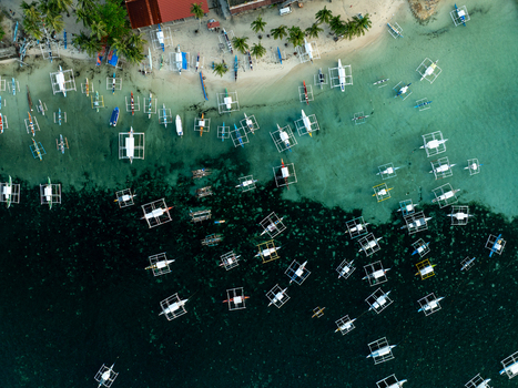 Aerial view of traditional outrigger boats anchored in the clear turquoise waters along the sandy coastline of Siargao Philippines. Aerial view of traditional outrigger boats anchored in the clear turquoise waters along the sandy coastline of Siargao Philippines.