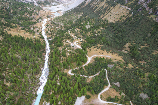 Aerial view of the Ferpecle glacier valley with the winding glacial stream surrounding pine forests and rugged mountain peaks in Evolene Valais Switzerland. Aerial view of the Ferpecle glacier valley with the winding glacial stream surrounding pine forests and rugged mountain peaks in Evolene Valais Switzerland.