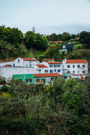 View of bright white and green buildings nestled among dense green trees with red tile roofs under an overcast sky Furnas Azores Portugal.