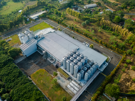 Aerial view of an industrial facility featuring large storage silos and a warehouse building surrounded by lush greenery in Semarang Regency Central Java Indonesia. Aerial view of an industrial facility featuring large storage silos and a warehouse building surrounded by lush greenery in Semarang Regency Central Java Indonesia.