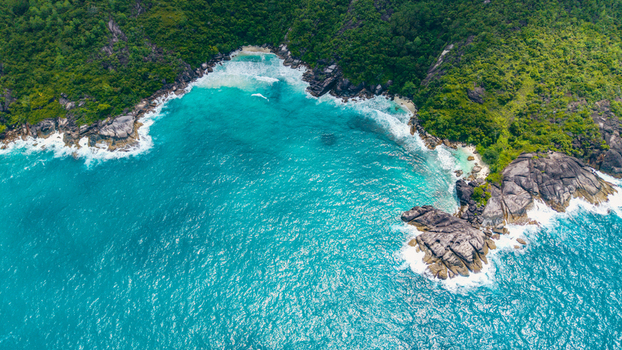 Aerial view of Anse Soleil Beachcomber Hotel with lush green hills rocky outcrops and turquoise waters in Mahe Baie Lazare Seychelles.