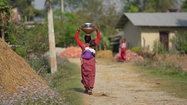View of a woman carrying a child and a pot in a village Nepal. View of a woman carrying a child and a pot in a village Nepal.