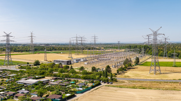 Aerial view of Amprion Umspannwerk substation with high voltage power lines and pylons spanning across agricultural fields and rural landscape in Pfungstadt Hessen Germany.