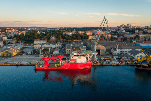 Aerial view of Uljanik Shipyard with a red vessel docked at the pier large cranes industrial buildings and the city of Pula in the background Pula Croatia. Aerial view of Uljanik Shipyard with a red vessel docked at the pier large cranes industrial buildings and the city of Pula in the background Pula Croatia.