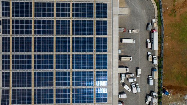 Aerial view of a large warehouse roof covered with a grid of solar panels with trucks parked in the loading area below in Bhiwandi Maharashtra India. Aerial view of a large warehouse roof covered with a grid of solar panels with trucks parked in the loading area below in Bhiwandi Maharashtra India.