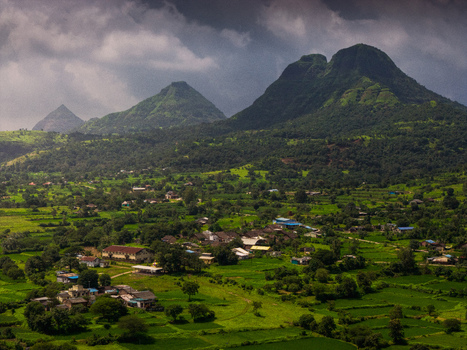 Aerial view of a small village nestled in the lush green landscape of the Western Ghats with rolling hills and dramatic cloudy skies in Maharashtra India. Aerial view of a small village nestled in the lush green landscape of the Western Ghats with rolling hills and dramatic cloudy skies in Maharashtra India.
