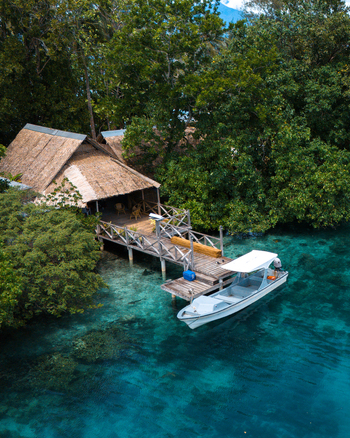 Aerial view of a boat peacefully moored at a wooden dock near a thatched roof hut embraced by the lush greenery of the islands Gizo Western Province Solomon Islands. Aerial view of a boat peacefully moored at a wooden dock near a thatched roof hut embraced by the lush greenery of the islands Gizo Western Province Solomon Islands.