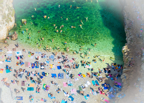 Aerial view of Lama Monachile beach with people swimming in turquoise water and sunbathing on the pebble shore surrounded by rocky cliffs in Polignano a Mare Apulia Italy. Aerial view of Lama Monachile beach with people swimming in turquoise water and sunbathing on the pebble shore surrounded by rocky cliffs in Polignano a Mare Apulia Italy.