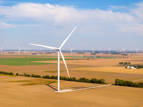 Aerial view of wind turbines in a vast agricultural landscape with golden fields and green patches under a blue sky in Wolcott Indiana United States.
