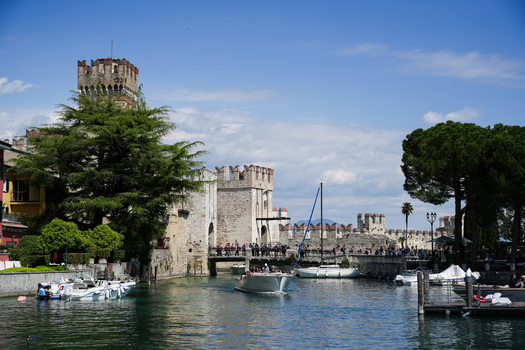 View of the medieval Scaligero Castle with its stone towers and bridge crowded with people over the blue waters of Lake Garda in Sirmione Lombardy Italy.
