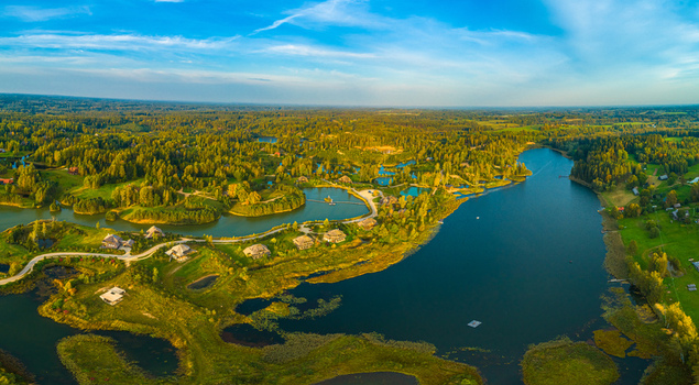 Aerial view of a serene landscape featuring a large lake winding roads lush green forests and scattered houses during the golden hour in Latvia. Aerial view of a serene landscape featuring a large lake winding roads lush green forests and scattered houses during the golden hour in Latvia.