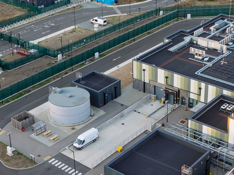 Aerial view of a modern data center facility featuring industrial rooftops a large water tank and a white van parked in the secure compound in the United Kingdom. Aerial view of a modern data center facility featuring industrial rooftops a large water tank and a white van parked in the secure compound in the United Kingdom.