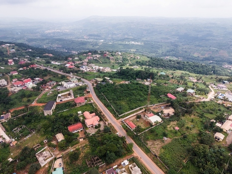 Aerial view of residential houses a winding road and a communication tower set amidst lush green hills and vegetation in Ghana. Aerial view of residential houses a winding road and a communication tower set amidst lush green hills and vegetation in Ghana.
