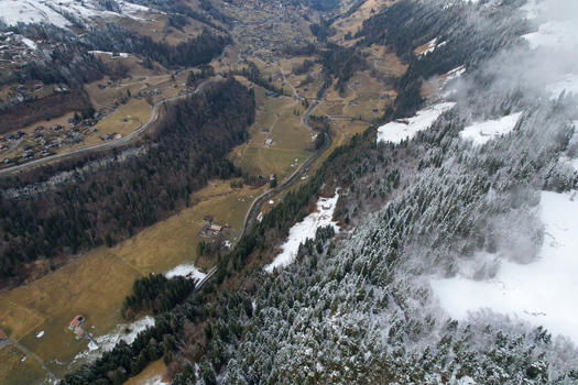 Aerial view of Les Rives area with snow covered pine forests winding mountain roads and traditional chalets in a deep alpine valley Champery Valais Switzerland.