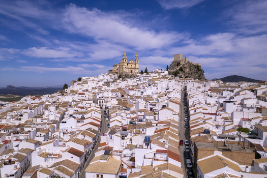 Aerial view of Olvera a white village in Andalusia featuring its hilltop church and castle overlooking dense traditional white houses under a blue sky. Olvera Andalusia Spain. Aerial view of Olvera a white village in Andalusia featuring its hilltop church and castle overlooking dense traditional white houses under a blue sky. Olvera Andalusia Spain.