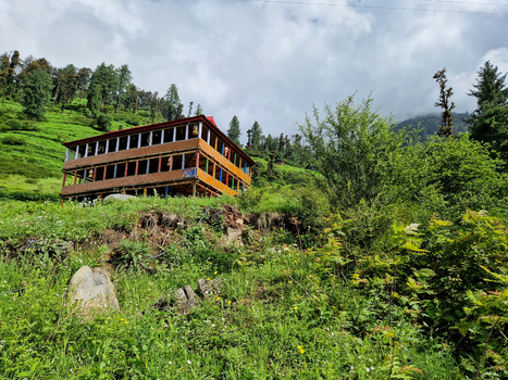 View of a traditional wooden house nestled on a lush green hillside in the Himalayan mountains of Malana Himachal Pradesh India.
