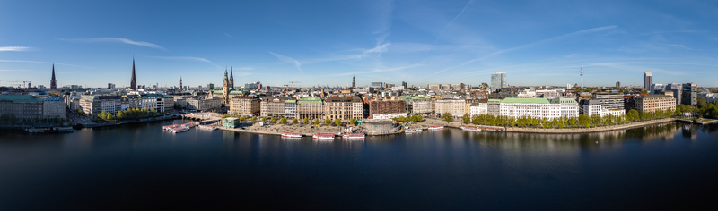 Aerial view of the Binnenalster lake waterfront with historic buildings church spires and boats along the promenade under a clear blue sky in Hamburg Hamburg Germany.