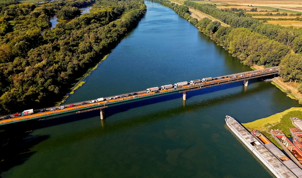 Aerial view of Smederevo bridge and shipyard with trucks and cars crossing the river barges moored in the shipyard and lush green riverbanks in Smederevo Podunavlje District Serbia.